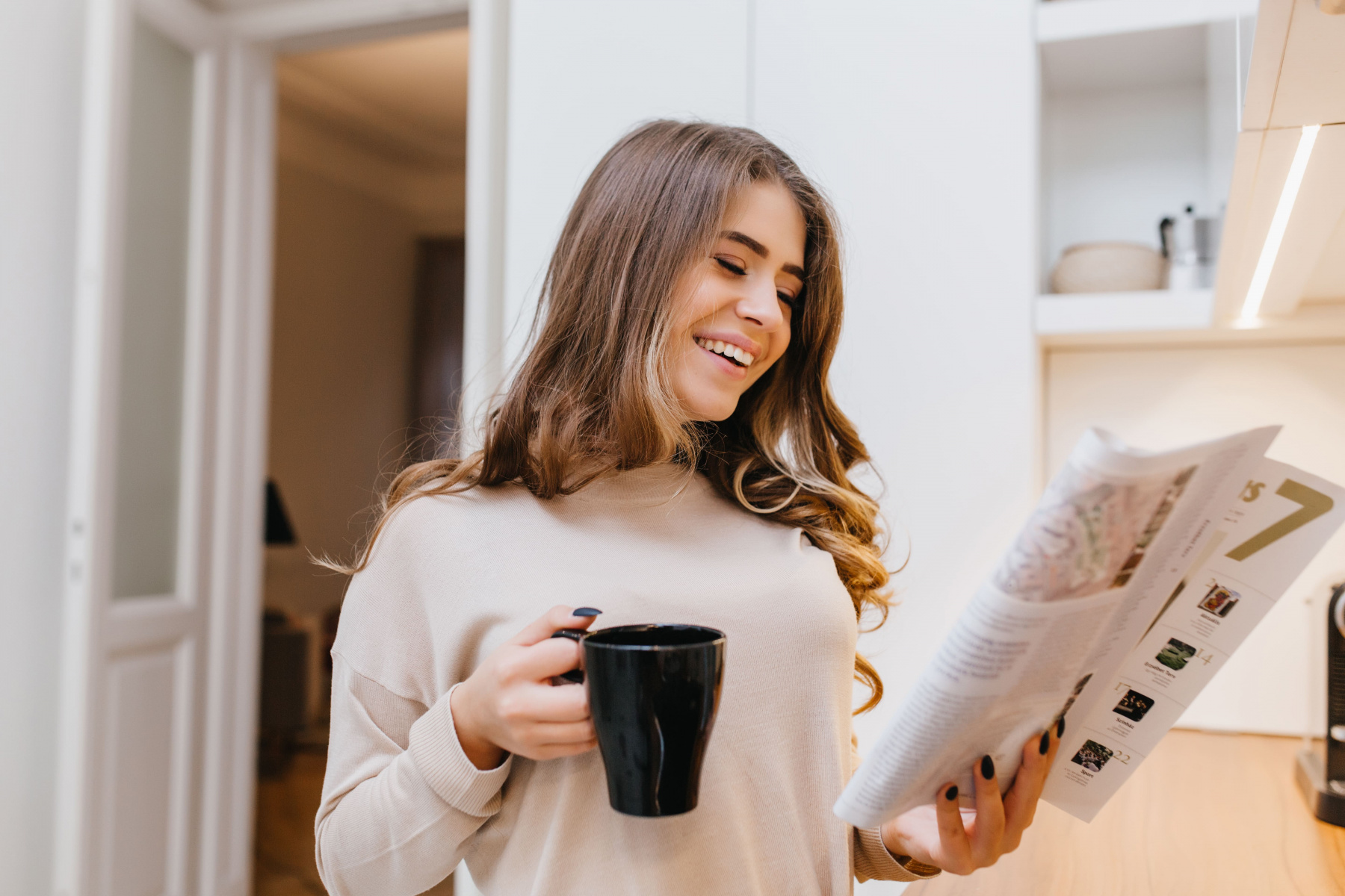 glad-white-woman-beige-attire-reading-news-kitchen-while-drinking-coffee.jpg