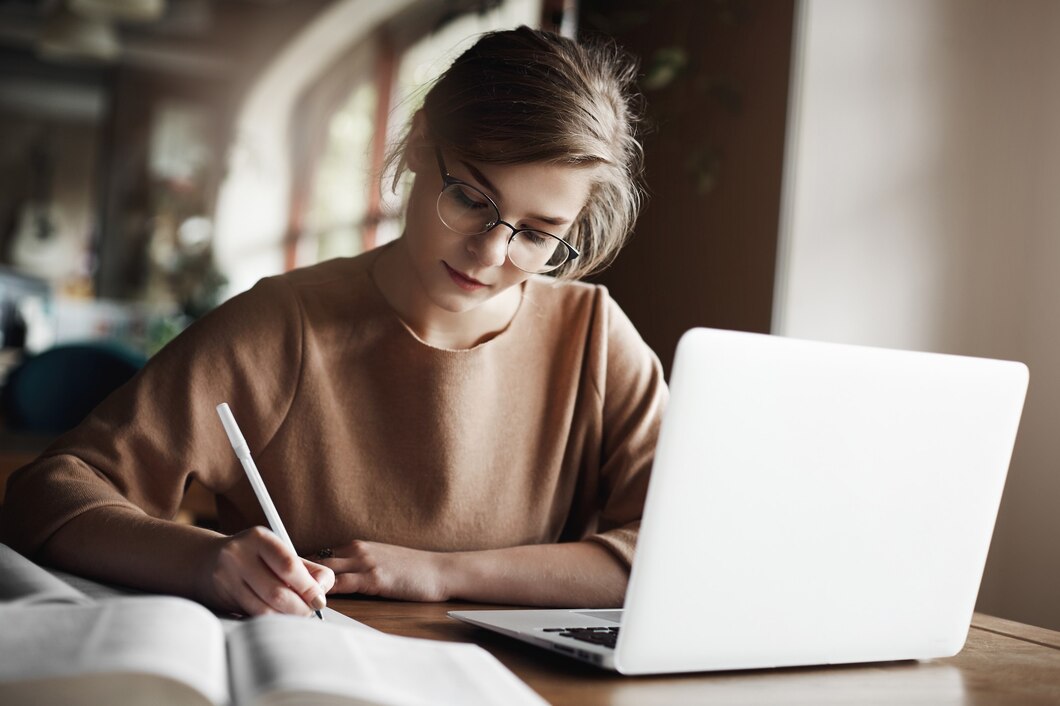 hardworking-focused-woman-trendy-glasses-concentrating-writing-essay-sitting-cozy-cafe-near-laptop-working-making-notes-carefully_197531-21320.jpg
